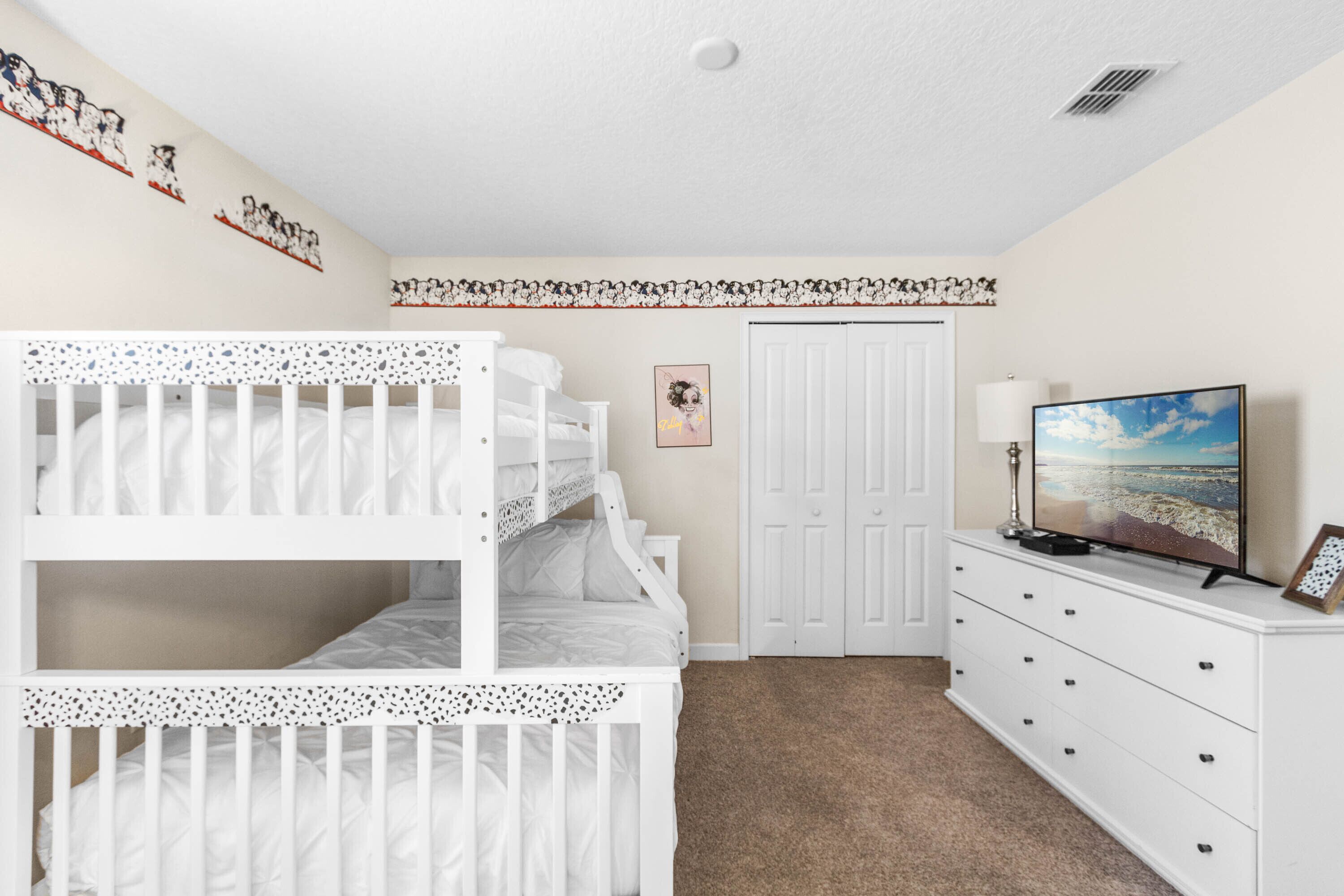 Une chambre avec un lit superposé, une commode, un téléviseur et une porte.