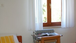 Une chambre à coucher avec un lit, un bureau en bois, une fenêtre avec des rideaux et un tableau accroché au mur.