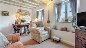 A cozy living room with a stone wall, a dining area with a table and chairs, a sofa, a television, and a window with curtains. - Vine Cottage - UKC4237 (Great Snoring, near Fakenham)