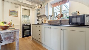 A kitchen with white cabinets, a wooden floor, a stove, a microwave, and a window with a view. - Vine Cottage - UKC4237 (Great Snoring, near Fakenham)