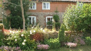 A brick house with a tiled roof, surrounded by a garden with various plants and flowers. - Vine Cottage - UKC4237 (Great Snoring, near Fakenham)