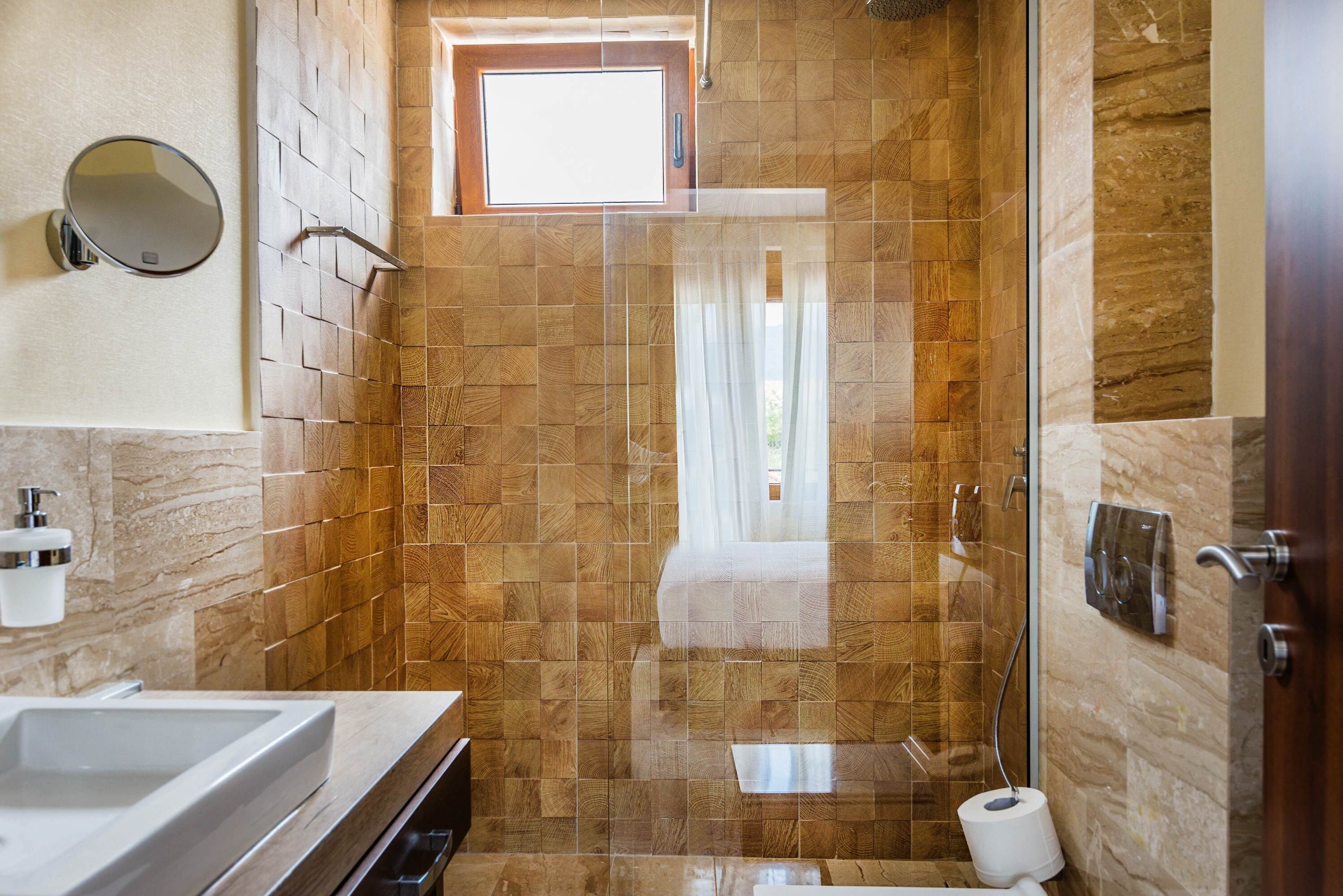 A bathroom with a large sink, a mirror, a shower with a glass door, and a window.