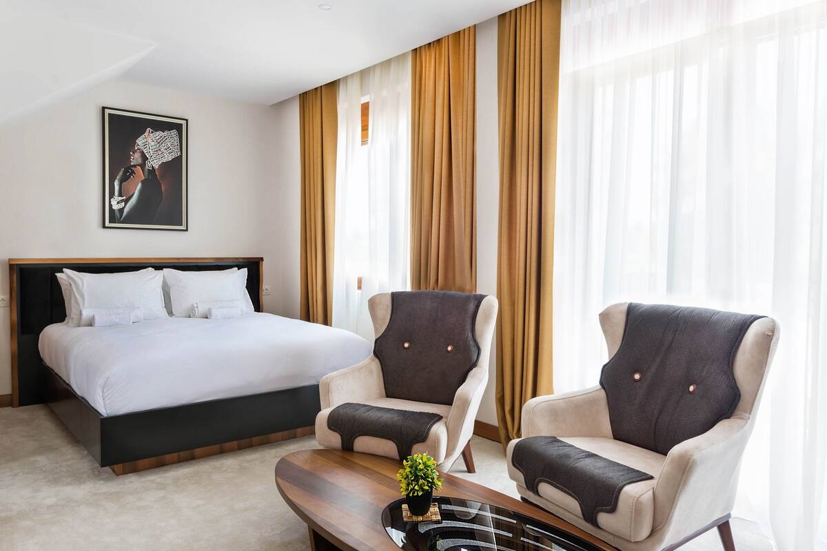 A hotel room with a bed, two armchairs, a coffee table, and a painting on the wall.