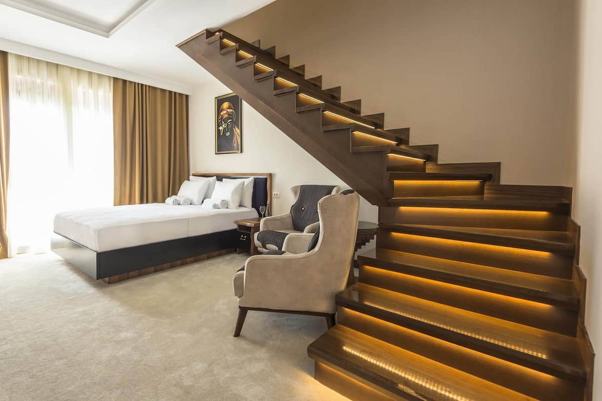 A bedroom with a large bed, a chair, and a staircase with illuminated steps.