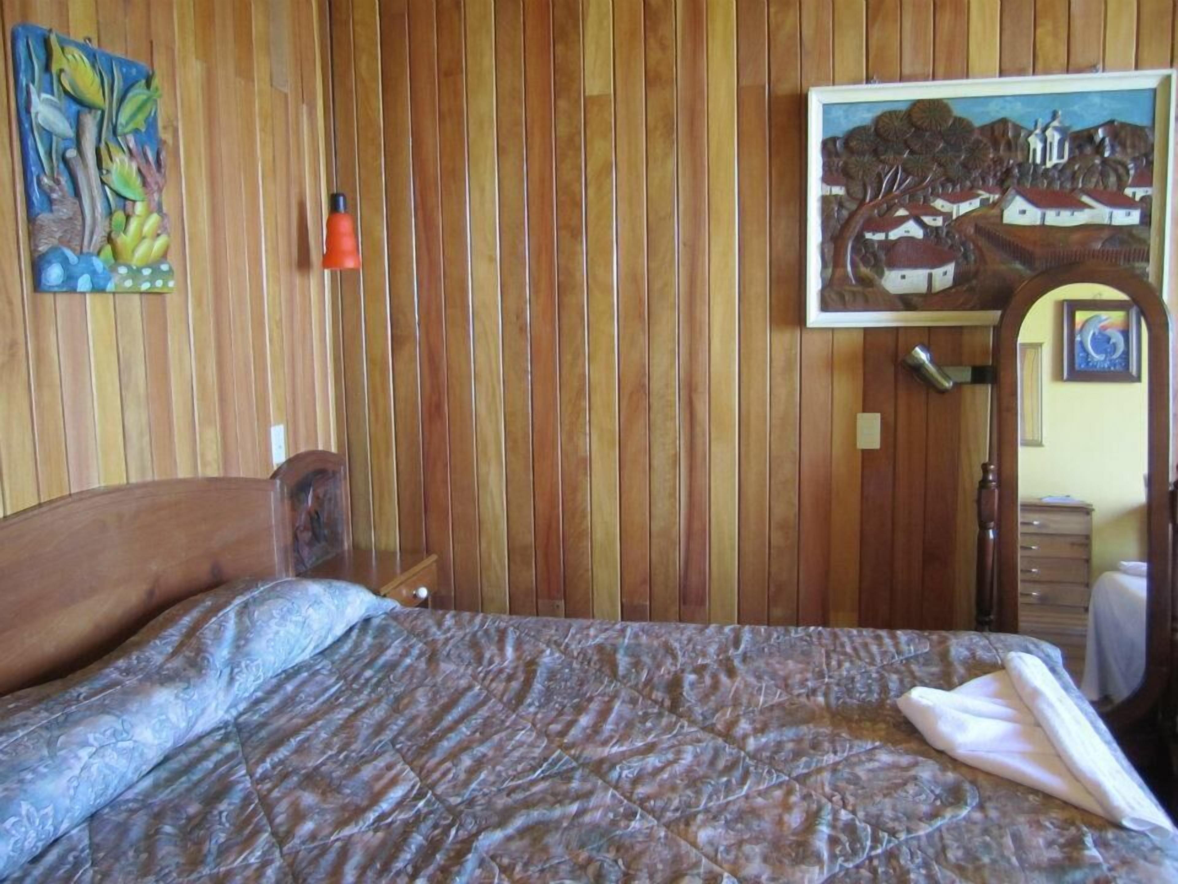 Ein Schlafzimmer mit einer Wand aus Holzlatten, einem Bett mit gemustertem Überwurf, einem Gemälde und einem kleinen Tisch mit einer Lampe.