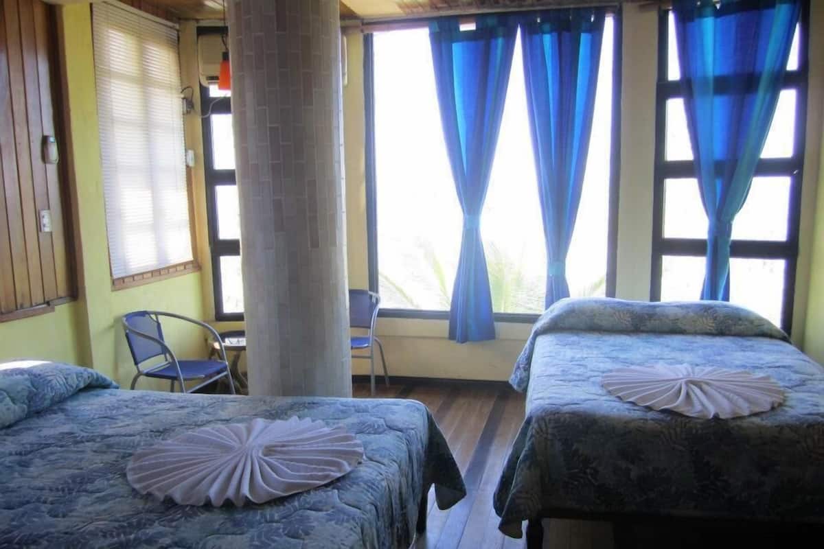 A room with two beds, a chair, and a window with blue curtains.