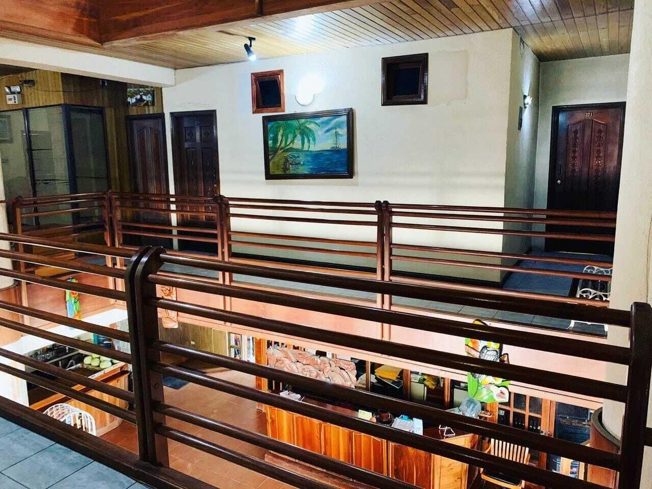 Um hall de hotel com guarda-corpo de madeira, uma pintura de uma paisagem praiana e vista para o andar inferior.
