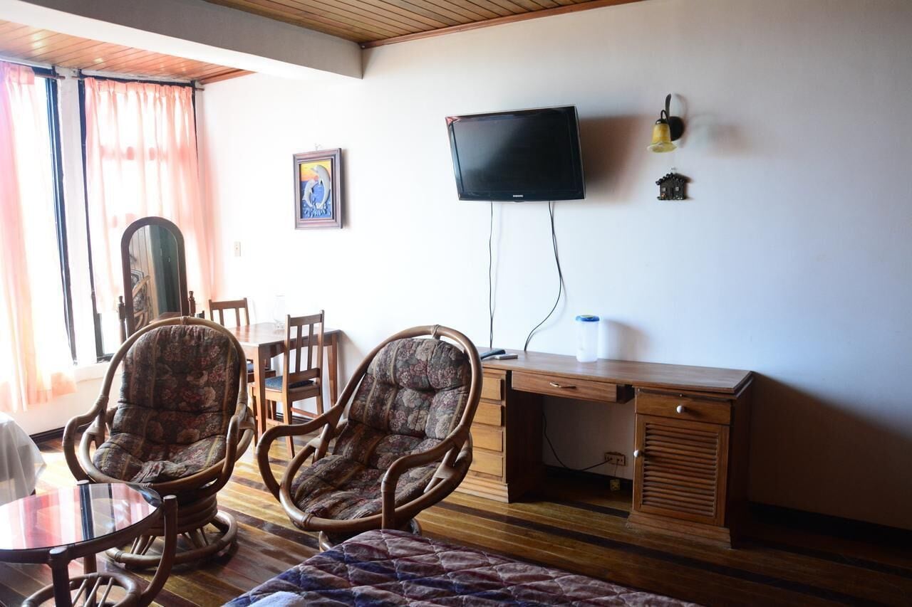 Una habitación con dos mecedoras, un escritorio de madera, un televisor y una lámpara pequeña.