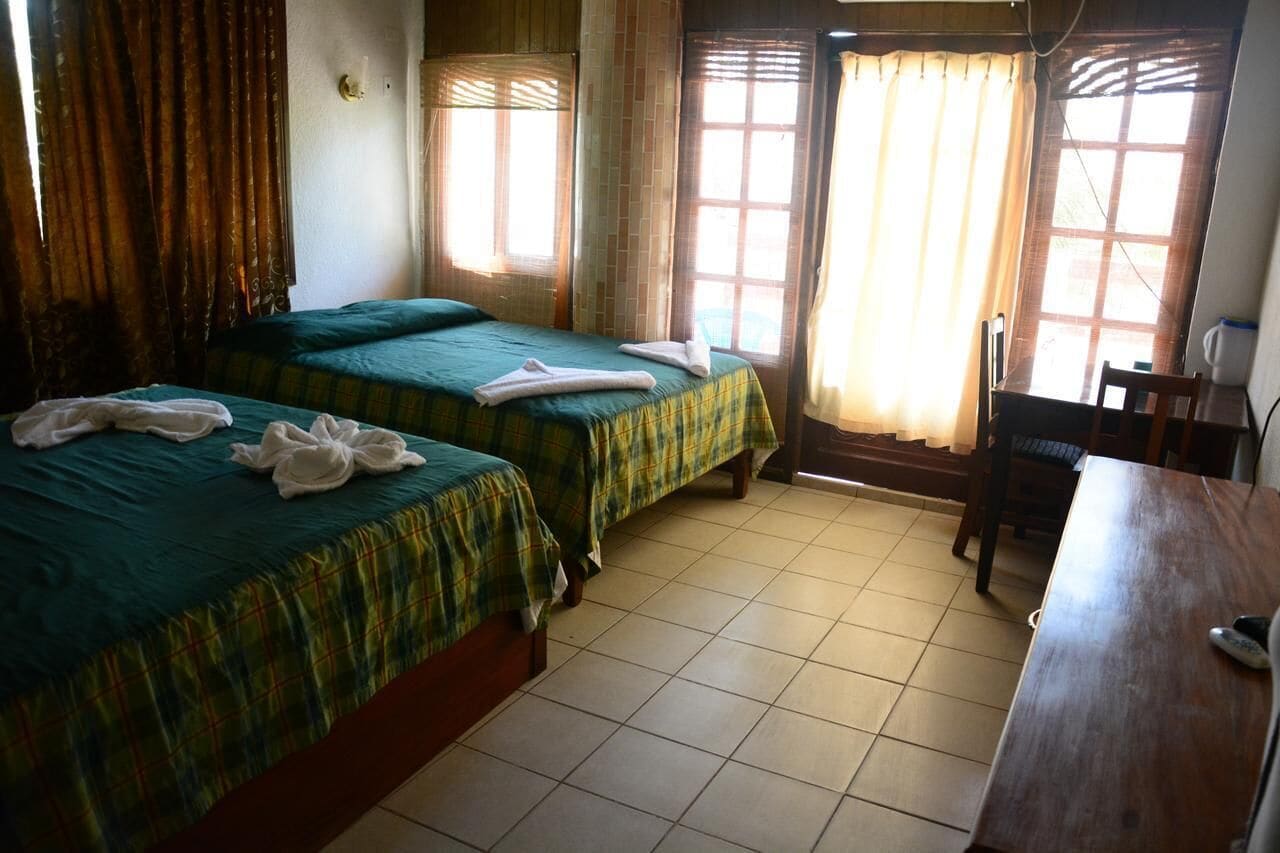 Une chambre d’hôtel avec deux lits, un bureau en bois et une fenêtre avec des rideaux.