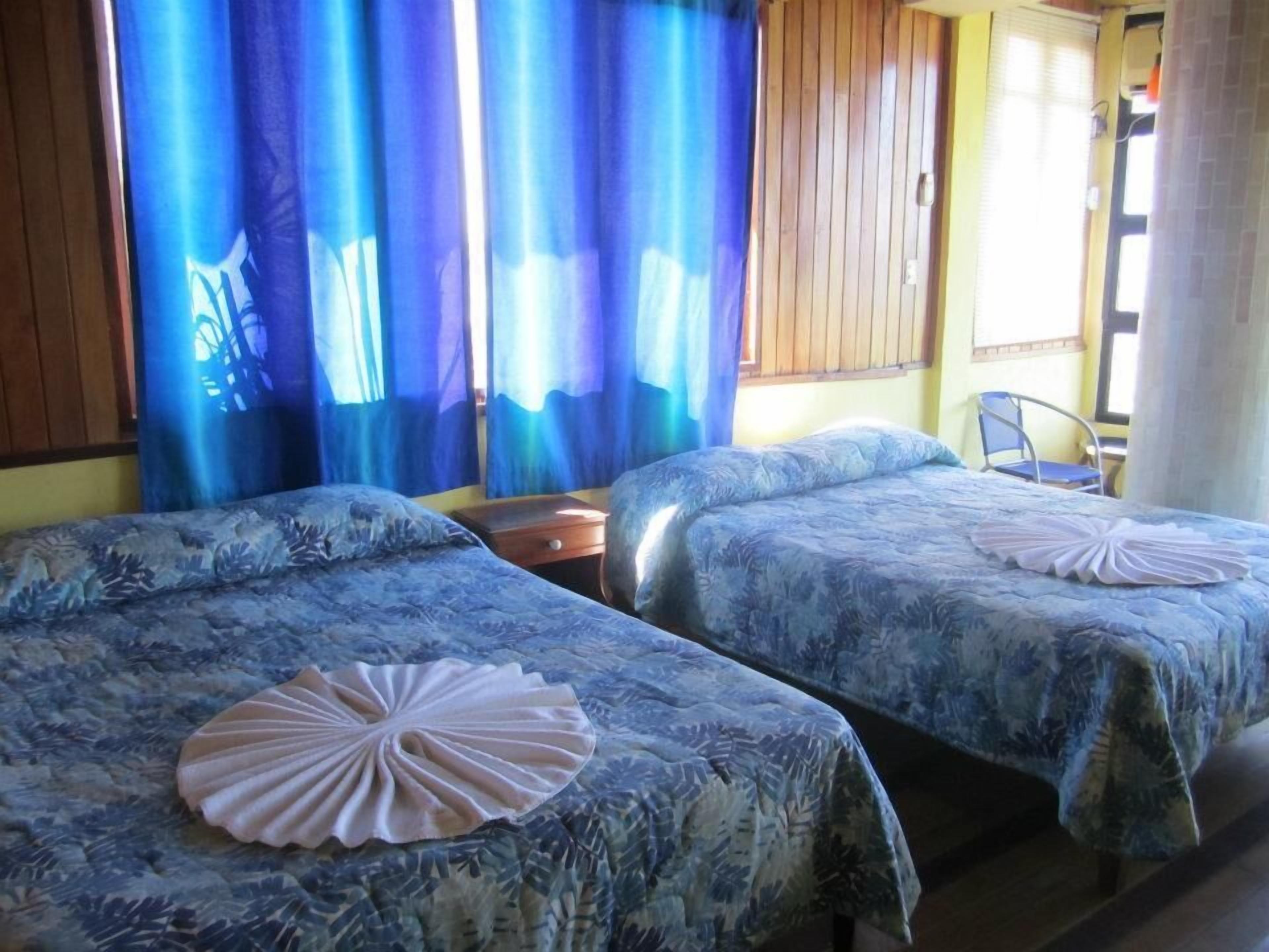 Ein Zimmer mit zwei Betten, beide mit floralem Bettbezug und einem dekorativen Kissen. Zwischen den Betten steht ein Nachttisch aus Holz, und in der Ecke ist ein Stuhl zu sehen.