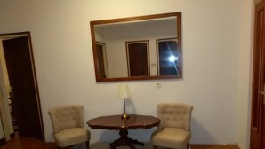 Ein Zimmer mit einem runden Holztisch, zwei Sesseln, einem weißen Teppich und einem großen Spiegel an der Wand.