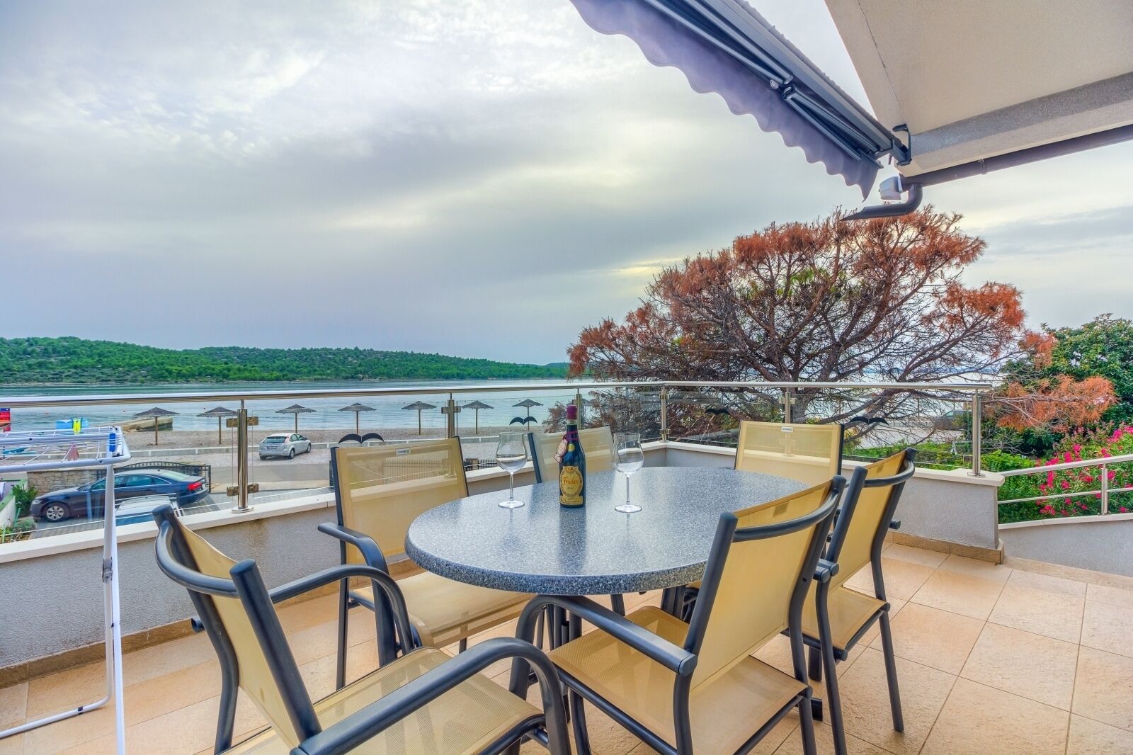 Uma varanda com mesa e cadeiras redondas, com vista para um corpo de água e um estacionamento.