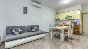 A compact living space with a sofa, dining table, chairs, a kitchen area, and an air conditioning unit. - Apartment in Pirovac with Seaview, Terrace, Air condition, WIFI (4925-2) (Pirovac)