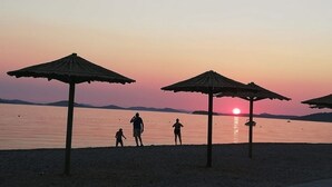 A beach scene with umbrellas and people at sunset. - Apartment in Pirovac with Seaview, Terrace, Air condition, WIFI (4925-2) (Pirovac)