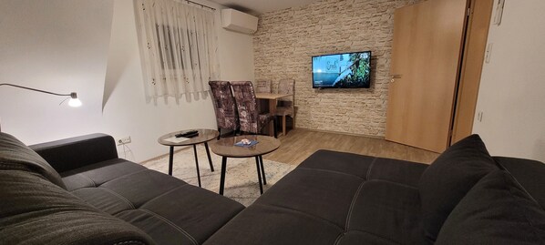 A living room with a stone wall, a TV mounted on it, a sofa, a small table, and a lamp.