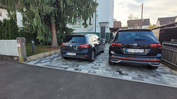 Deux voitures garées dans une allée, avec une clôture blanche et un bâtiment en arrière-plan.