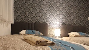 Une chambre d’hôtel avec deux lits, une literie à motifs, une tête de lit et un mur orné d’un motif décoratif.