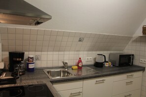 A kitchen with a stove, sink, and microwave. There are cabinets, a coffee maker, and a bottle of dish soap.
