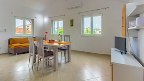 A modern apartment with a dining area, a sofa, a TV, and large windows.