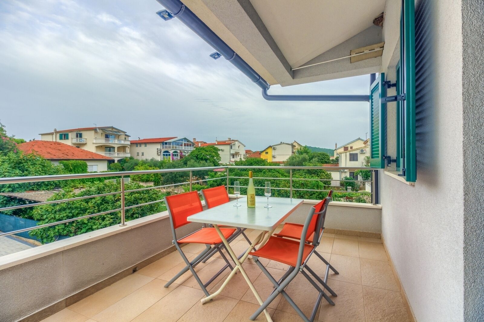 Varanda com mesa e cadeiras, com vista para uma área residencial com casas e vegetação.