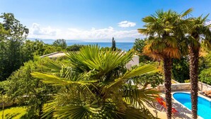 A poolside view with a clear view of the sea, surrounded by lush greenery and palm trees. - Apartment in Njivice with Seaview, Balcony, Air condition, WIFI (4930-1) (Njivice)