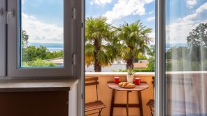 A balcony with a table, two chairs, a potted plant, and a view of the sea and mountains. - Apartment in Njivice with Seaview, Balcony, Air condition, WIFI (4930-1) (Njivice)