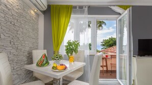 A modern room with a stone wall, a dining table with chairs, a small kitchen area, and a view of the sea. - Apartment in Njivice with Seaview, Balcony, Air condition, WIFI (4930-2) (Njivice)