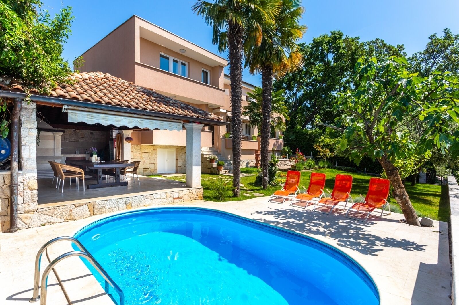 Ein Pool mit Liegestühlen, eine Terrasse mit Tisch und Stühlen sowie ein Gebäude mit einem Ziegeldach.