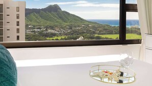 A hotel room with a large window offering a view of a mountain and a coastal town. - Ocean-view condo w/ pool near Waikiki Beach (Honolulu)