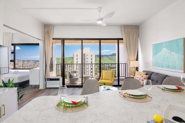 A modern hotel room with a dining area, a balcony with a view, and a large window.