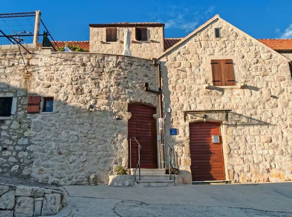 Un edificio de piedra con dos puertas rojas, un ventanal pequeño y una escalera que lleva a la entrada.
