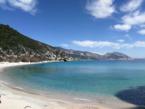 A beach with clear turquoise water, white sandy shore, and a mountainous backdrop.