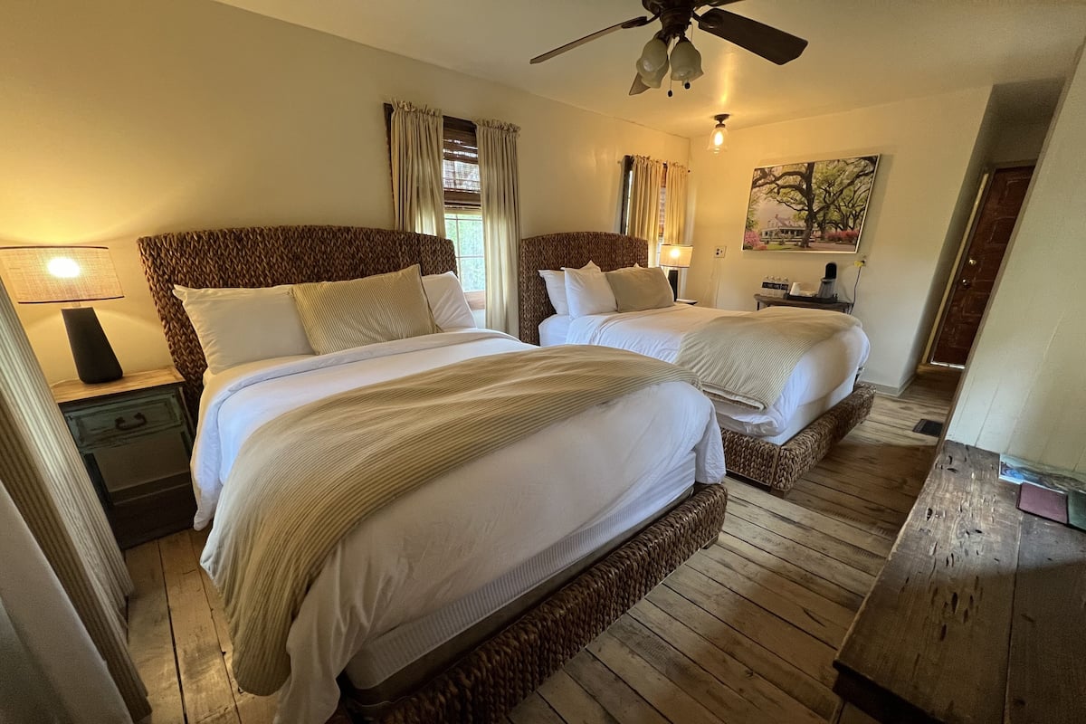 Une chambre d’hôtel avec deux lits, un plancher en bois, un ventilateur de plafond et un tableau au mur.