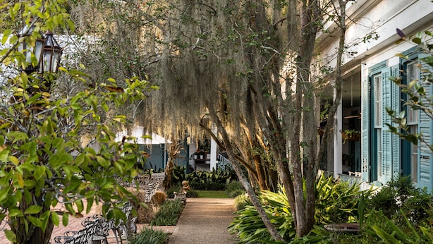 A garden pathway leading to a building with blue shutters and a statue in the center.