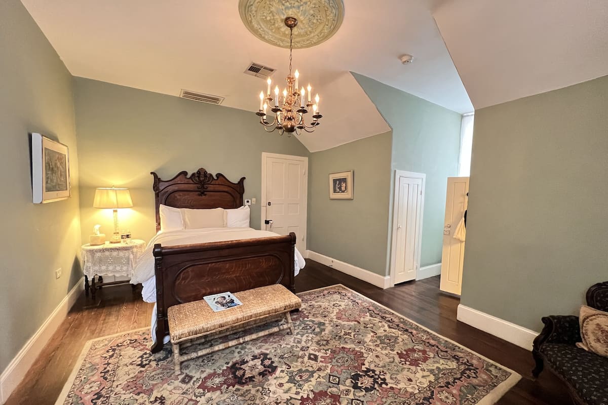 Une chambre à coucher avec un grand lit, un lustre, un tapis à motifs et un banc en bois.