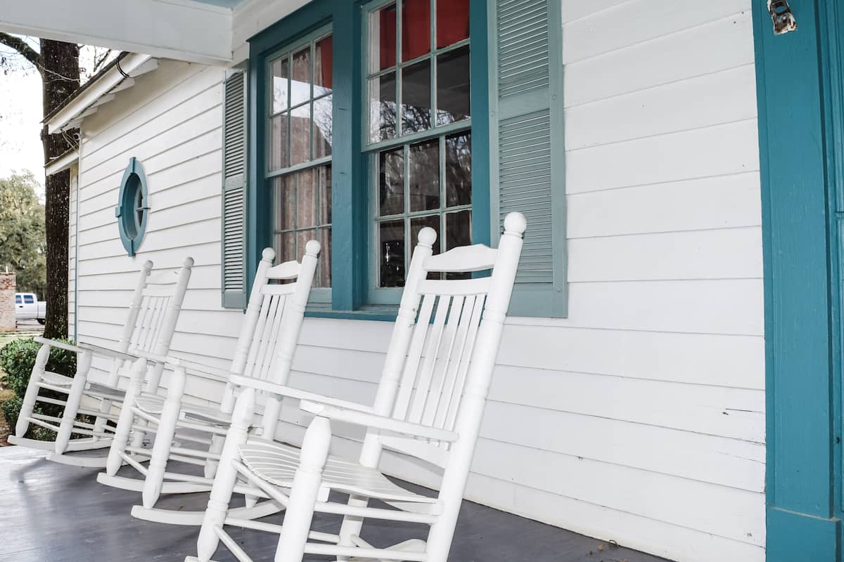 Une véranda avec des fauteuils à bascule blancs et une porte de couleur turquoise.