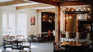 A restaurant with wooden beams, exposed brick, and hanging light bulbs. Tables are set with plates and cutlery.