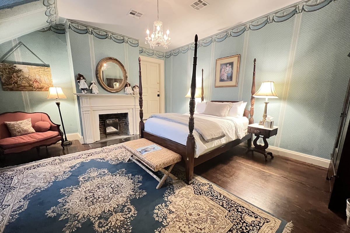 Un lit à baldaquin, une cheminée, un canapé rouge et un tapis à motifs.
