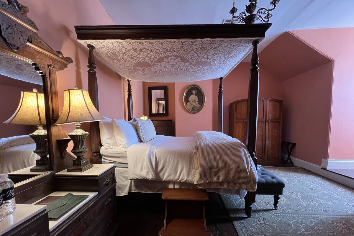 Un lit à baldaquin, une table de chevet avec une lampe, une commode en bois et un miroir.