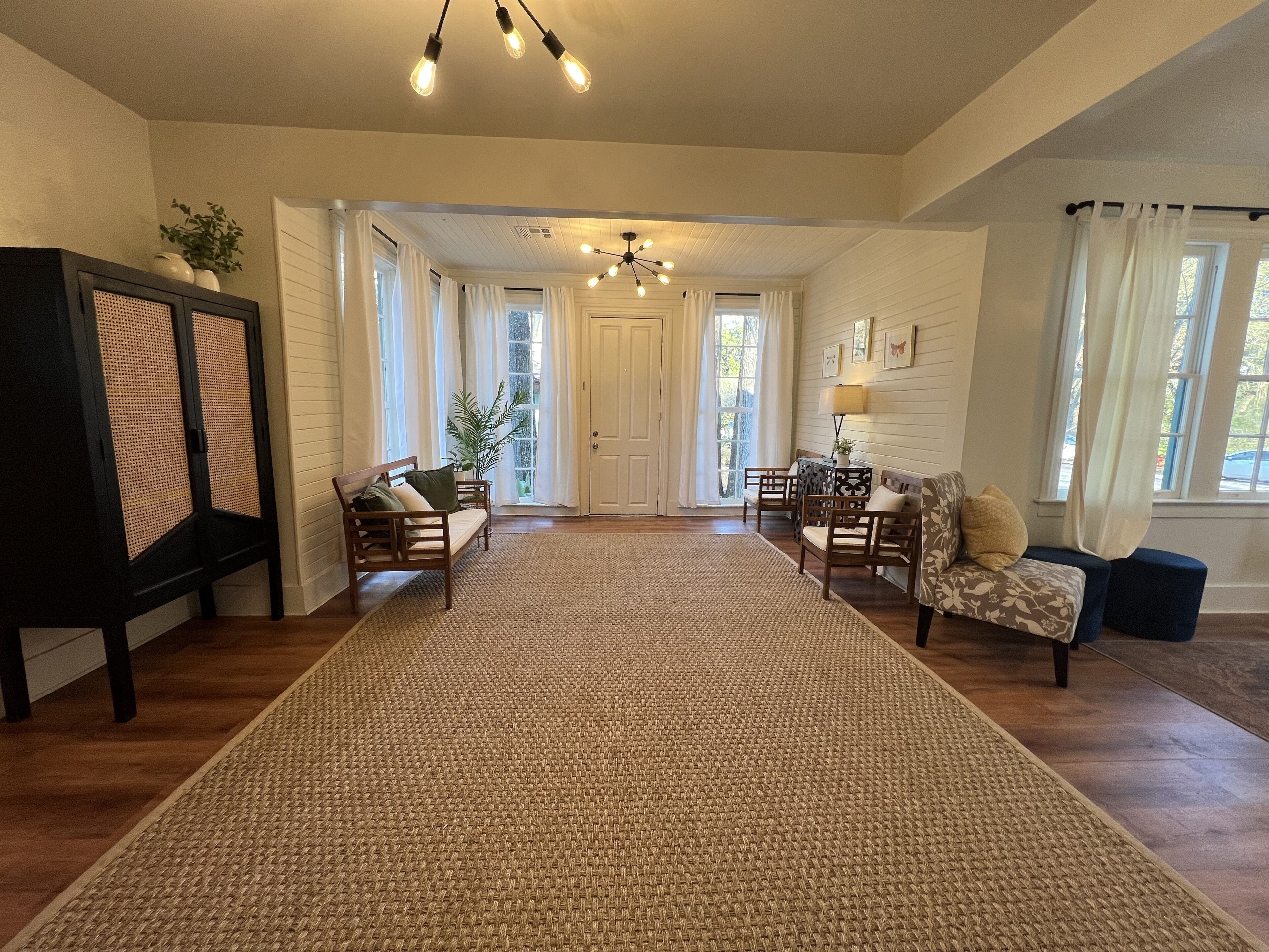Un salon spacieux agrémenté d’un grand tapis tissé, de meubles en bois et d’un luminaire suspendu au plafond.