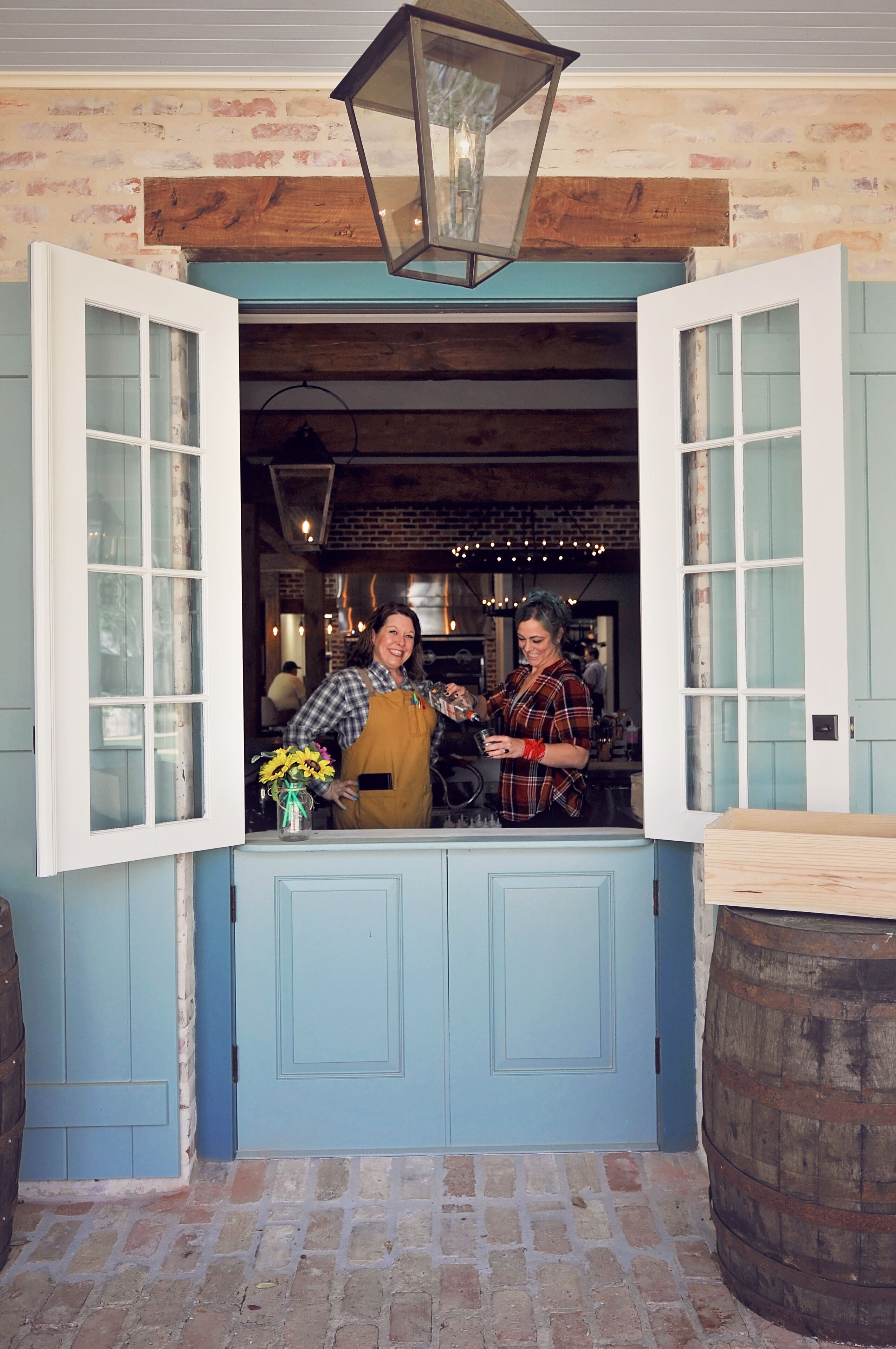 A person standing at a counter with open windows, a wooden barrel, and a brick wall.