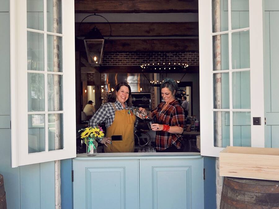 A person standing at a counter with open windows, a wooden barrel, and a brick wall.