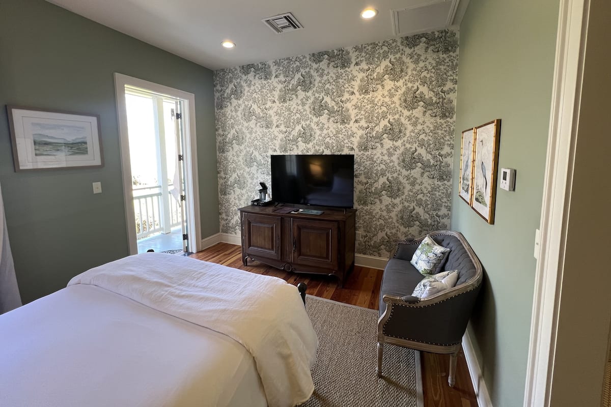 Une chambre à coucher avec un lit, un téléviseur posé sur un meuble, une chaise et un mur décoré d’un motif.
