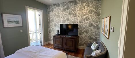A bedroom with a bed, a television on a cabinet, a chair, and a patterned wall.