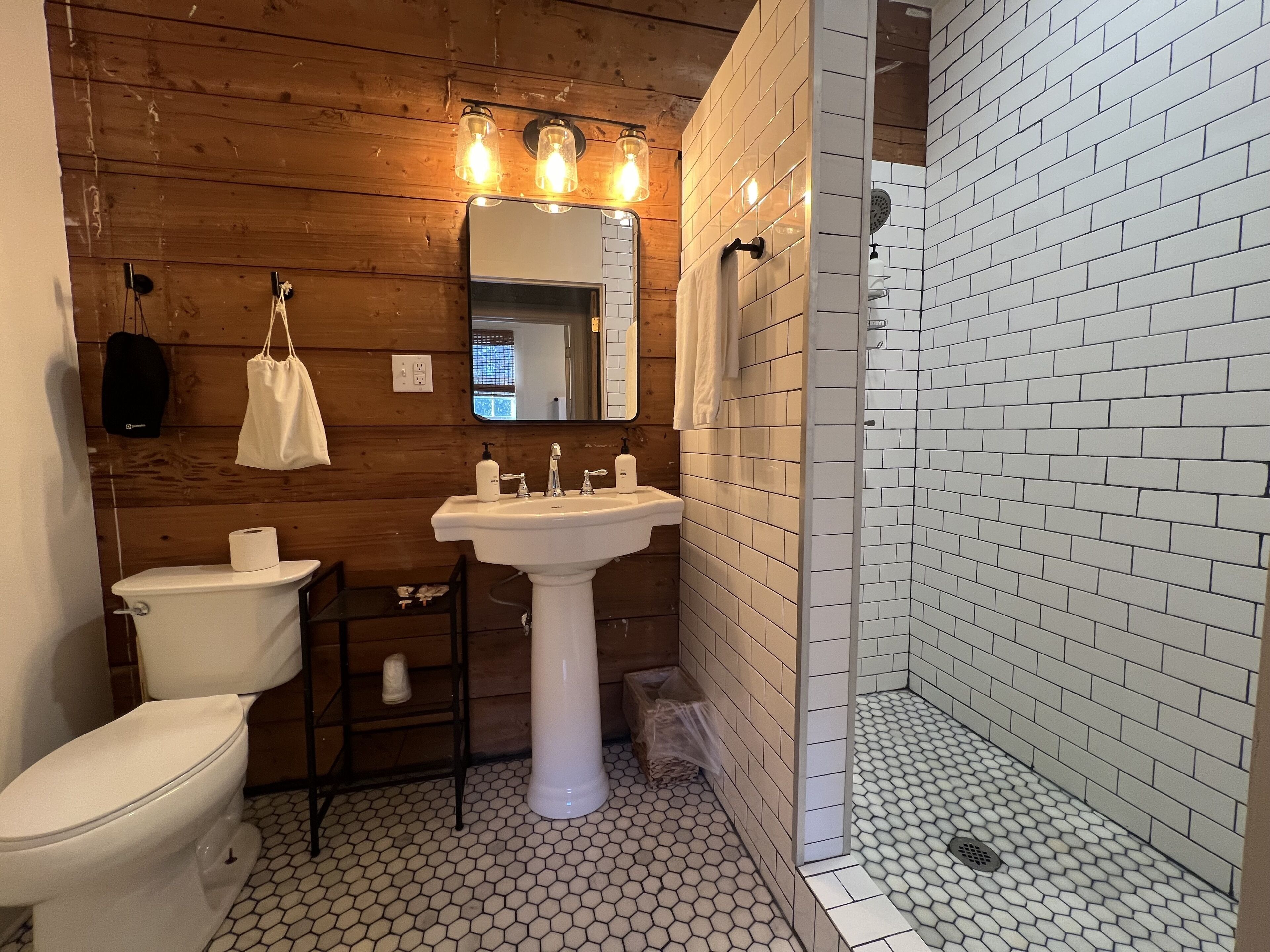 Un baño con pared de madera, un lavamanos blanco, un inodoro y una zona de ducha con azulejos blancos.