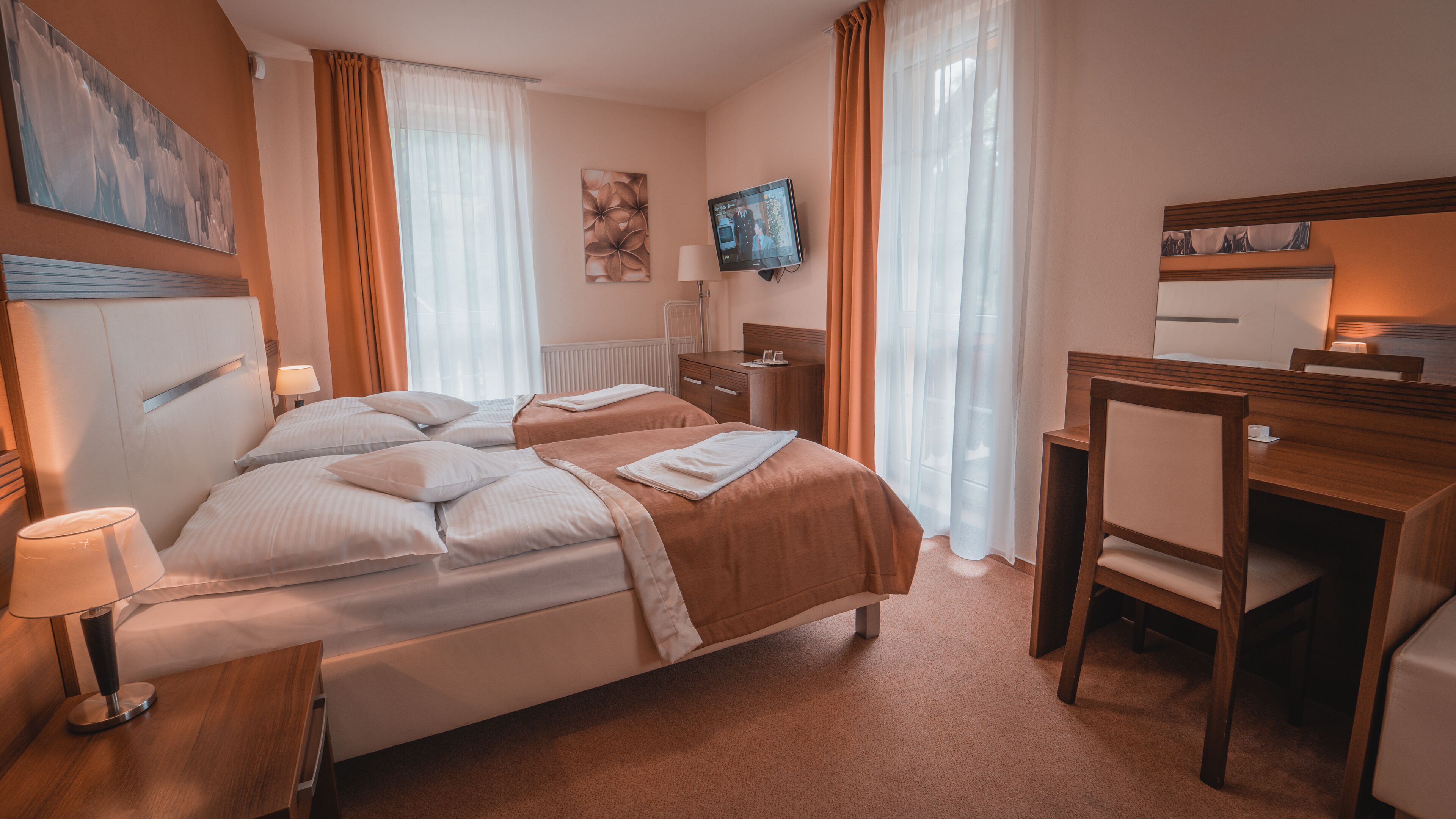 Habitación de hotel con cama, mesitas de noche, escritorio, silla, televisor y cortinas.