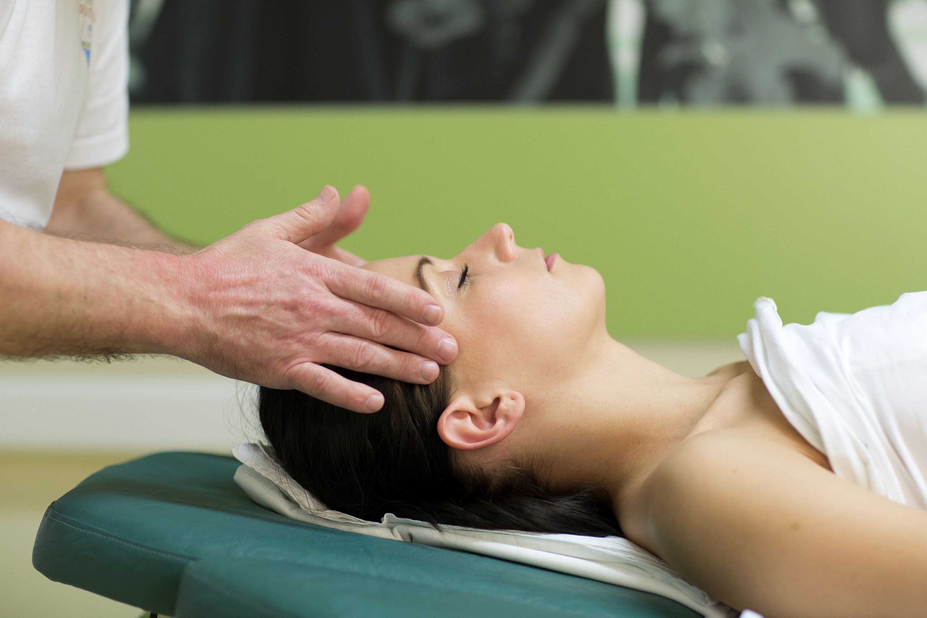 Une personne allongée sur une table de massage verte, en train de recevoir un massage de la tête.