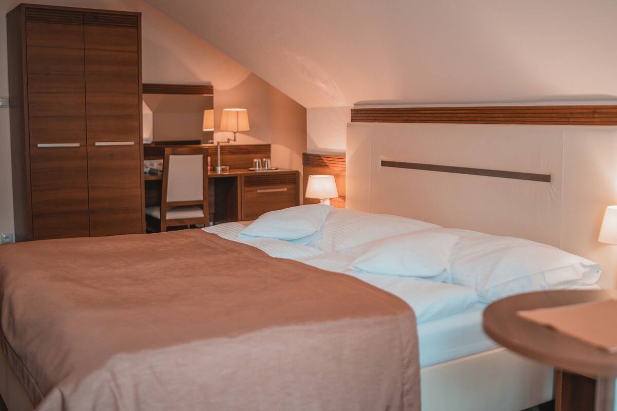 Habitación de hotel con una cama grande, un escritorio, una silla, un armario y dos lámparas de noche.