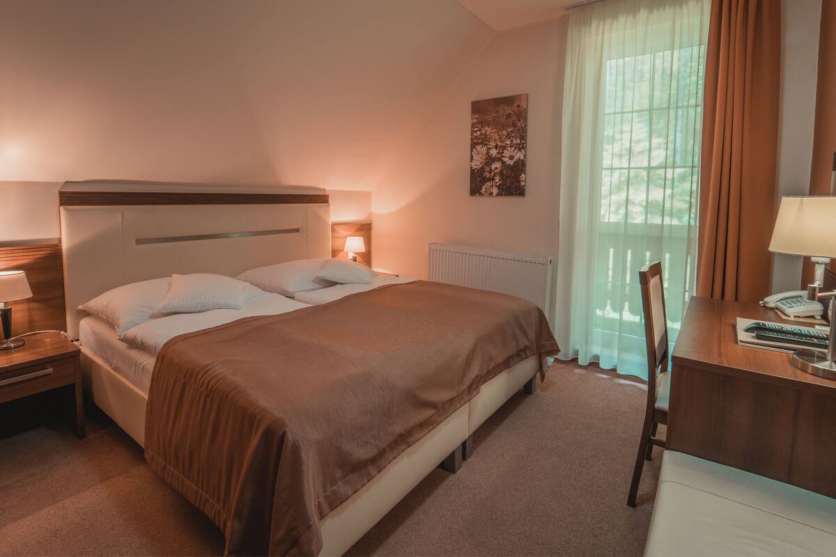 Habitación de hotel con cama, lámparas de noche, escritorio con teléfono y ventana con cortinas.