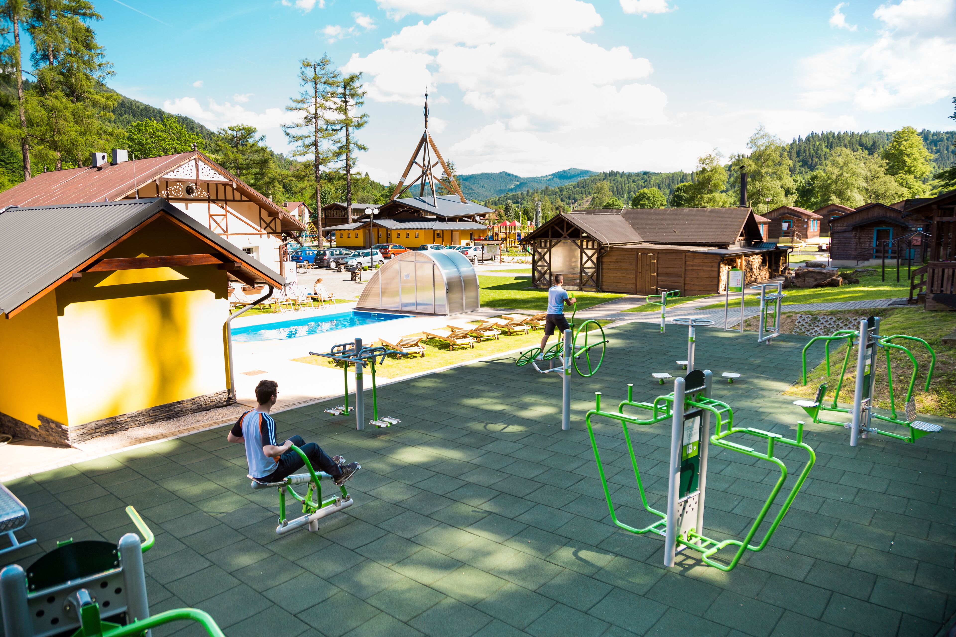 A hotel with outdoor exercise equipment, a pool, and a mountain backdrop.